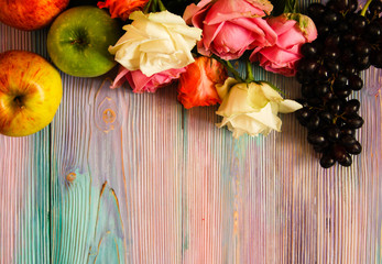 Colorful wooden background with roses, grapes and apples