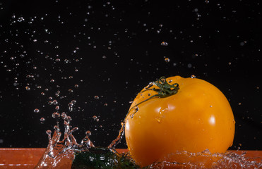 Yellow tomato and cucumber in water splashing.