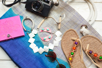 Flat lay of summer fashion with camera, slippers, sunglasses and other girl accessories on top of the bag on white wooden background