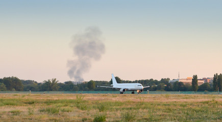 Fototapeta premium Smoke near airport with airplane taxiing on runway