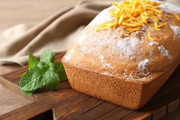 Cutting board with delicious citrus cake and zest on table