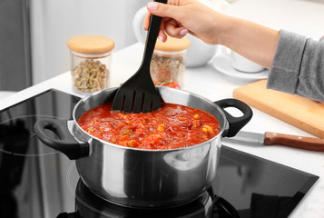 Woman cooking turkey chili on modern stove in kitchen