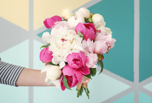 Female hand with bouquet of beautiful peony flowers on color background