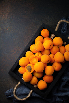 Delicious ripe apricots on a wooden stand on a dark black background. Selective focus. Top view. Cope space.