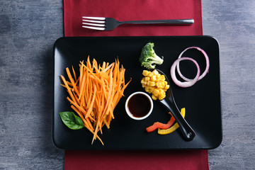 Black plate with delicious carrot salad and sauce on table