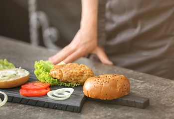 Obraz na płótnie Canvas Woman cooking tasty turkey burger at table