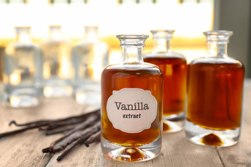 Bottles with aromatic extract and dry vanilla beans on table