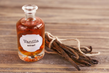 Bottle with aromatic extract and dry vanilla beans on table