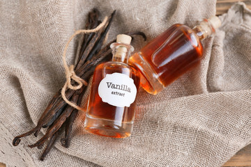 Bottles with aromatic extract and dry vanilla beans on napkin