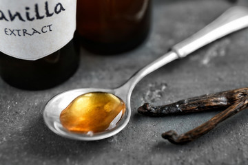 Spoon with aromatic extract and dry vanilla beans on table