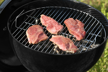 Tasty beefsteaks cooking on barbecue grill outdoors, close up
