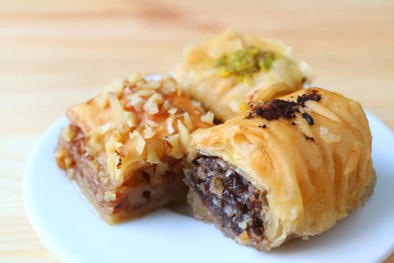 Closed up Three Types of Baklava Sweets on White Plate Served on Wooden Table, Blurred Background 