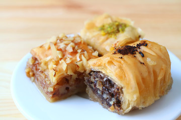 Closed up Three Types of Baklava Sweets on White Plate Served on Wooden Table, Blurred Background 