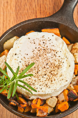 Sweet potato and turnip hash with turkey and fried egg, sprig of rosemary in a cast iron pan hot off the heat and resting on a wood cutting board