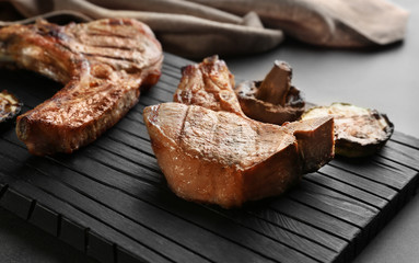 Board with grilled steaks and vegetables on grey table, close up