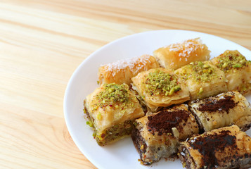 Many types of Baklava pastries on white plate served on wooden table, with free space for text and design 