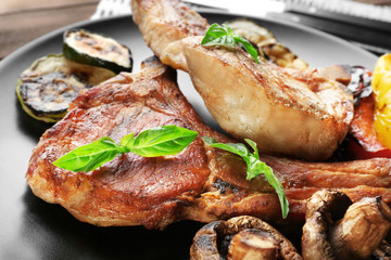 Plate with grilled steaks and vegetables on table, close up