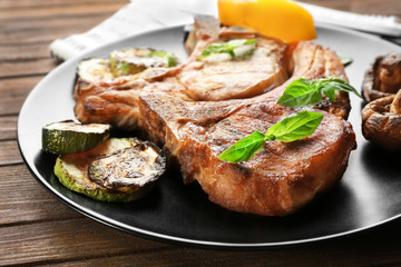 Plate with grilled steaks and vegetables on wooden table, close up