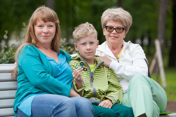 Family portrait with mother, young son with spinner and senior grandmother on bench in summer park