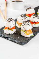 Trend hybrid food. Japanese Asian cuisine. Mini sushi-burgers, sandwiches with salmon, hayashi wakame, daikon, ginger, red caviar. White marble table, with chopsticks, soy sauce. Copy space