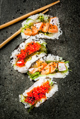 Trend hybrid food. Japanese Asian cuisine. Mini sushi-tacos, sandwiches with salmon, hayashi wakame, daikon, ginger, red caviar. Black stone table, with chopsticks, soy sauce. Copy space top view