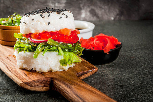 Trend hybrid food. Japanese Asian cuisine. Sushi-burger, sandwich with salmon, hayashi wakame, daikon, ginger, red caviar. Black stone table, with soy sauce. Copy space