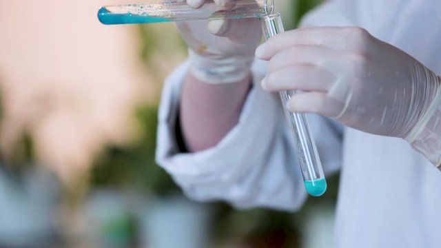 Scientist hand pouring a chemical solution from a laboratory glass test tube into a scientific cylinder with liquid for an experiment in a science research lab