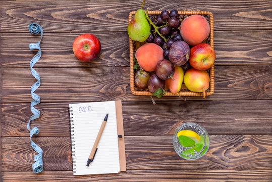 Top view notebook on the wooden table with Basket of different Fresh fruits, measuring tape, glass of waterwith lemon. Healthy lifestyle concept. Detox, diet. Selective focus. Copy space