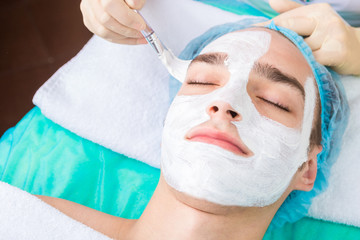 male cosmetology. Skin beauty care. The cosmetologist applies a mask for cleansing and moisturizing the patient's skin