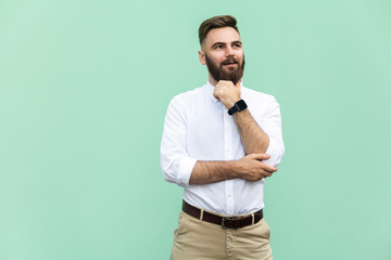 Thoughtful bearded businessman looking away while standing against light green wall. Studio shot