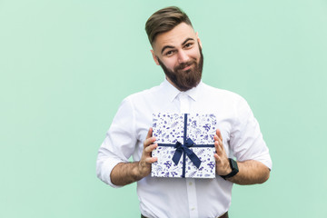 Gift with love. Interesting bearded young adult man with a gift box on light green background. Studio shot