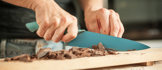 Woman hands chopping chocolate block for celebratory cake