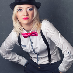 beautiful young woman wearing tophat, bow-tie and braces against grey background