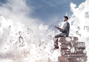 Man student on stack reading book and symbols flying around