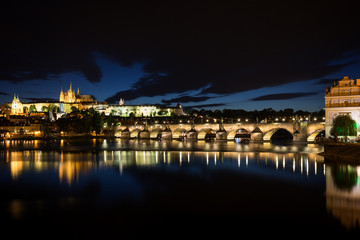 Obraz premium View of the lit Prague (Hradcany) Castle, Charles Bridge (Karluv most) and their reflections on the Vltava River in Prague, Czech Republic, at night.