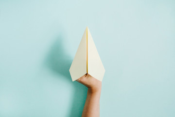 Fototapeta premium Women hand holding paper plane on pale blue background. Flat lay, top view.