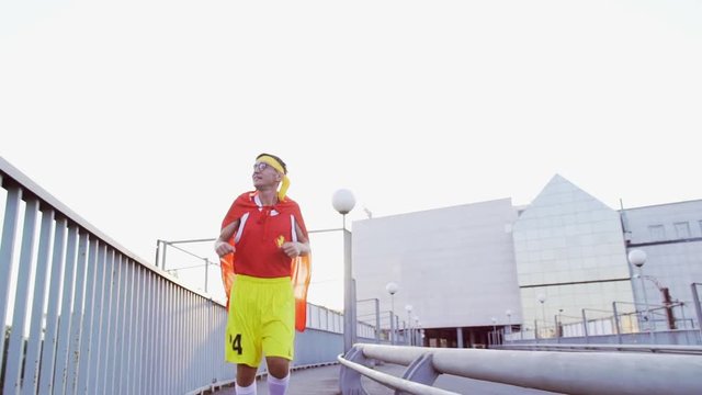 Funny thin guy in a superhero costume on a run on the bridge in the morning.