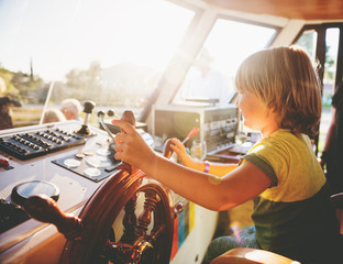 Cute little boy pretending to a be captain, child steering a ship at sunset