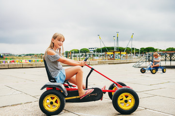 Two active little kids driving pedal race car. Outdoor summer activities for children