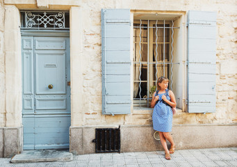 Pretty little girl tourist on the streets of Provence, Wearing blue gingham dress, sunglasses and backpack. Travel with children concept. Image taken in Arles, France