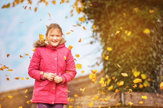 Funny little girl playing in autumn park, wearing bright red parka jacket