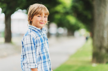 Outdoor fashion portrait of cute little 6 year old boy wearing blue plaid casual shirt