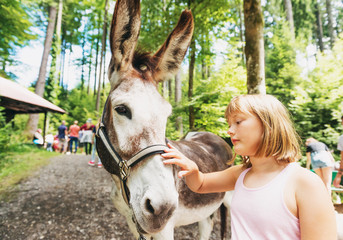 Little girl hiking with donkeys in summer camp for children