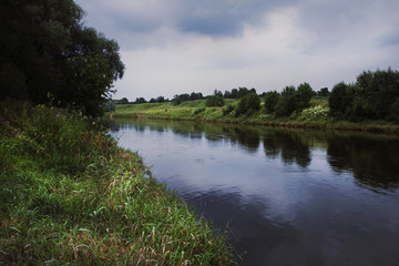 The river is dark blue with lush green grass and trees along the banks