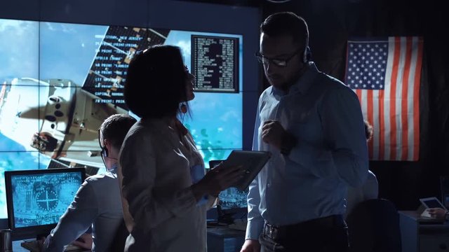 Side view of man and woman communicating in space flight control center. Some elements of this image furnished by NASA.