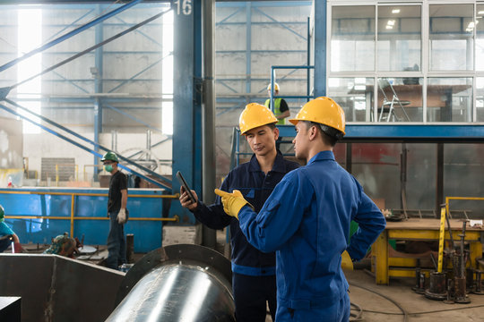 Asian experts checking information on tablet PC while supervising work in a modern factory