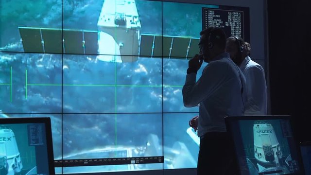 People in space mission control center managing spaceship undocking. Elements of this image furnished by NASA.