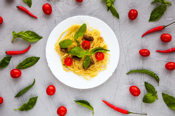 Spaghetti with beef meat slices, cherry tomatoes and basil leaves on white plate. Light grey marble stone surface for background with Chile peppers. Ideas for restaurant menu. Top view.
