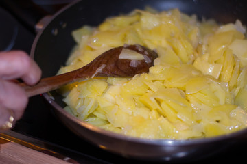 Old woman cooking traditional Spanish omelette with wooden spoon. Cooking potatoes in a pan. Old doman hand. Traditional food concept.