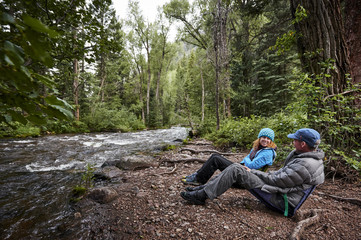 a man and woman sitting next to a mountain river